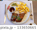 Grilled steak with roasted potatoes, dipping sauce, and pickles on a rustic plate 133650665