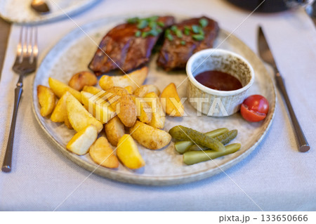 Grilled steak with roasted potatoes, dipping sauce, and pickles on a rustic plate 133650666