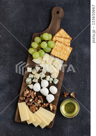 Gourmet cheese platter with crackers, grapes, walnuts, and honey on rustic dark background Gourmet cheese platter with crackers, grapes, walnuts, and honey on rustic dark background 133650667