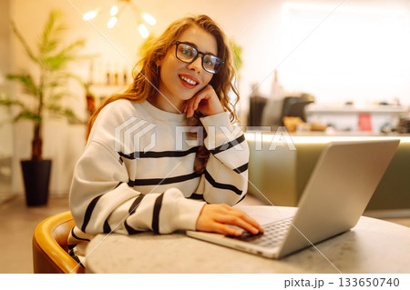 Portrait of a young woman sitting in a cafe at a laptop, working online, freelancing. Technologies. Portrait of a young woman sitting in a cafe at a laptop, working online, freelancing. Technologies. 133650740