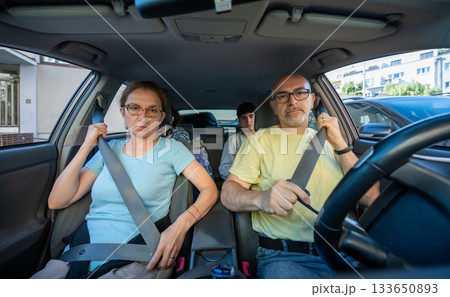 Berlin, Germany 10 August 2023. Car safety concept: a family is sitting in a car, in the foreground a middle-aged husband and wife are fastening their seat belts before driving off 133650893
