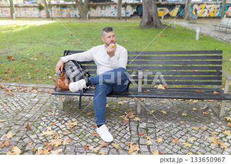 Male adult enjoying healthy snack sitting on park bench Male adult enjoying healthy snack sitting on park bench 133650967