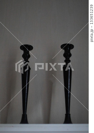 Two black candlesticks standing on the shelf. Two black candlesticks standing on the shelf. 133651239