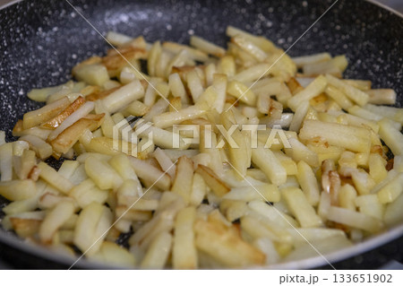 Potatoes cut into slices are deliciously fried in a frying pan. 133651902