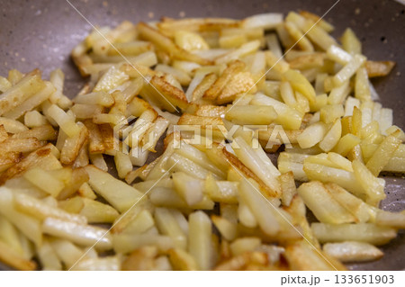 Potatoes cut into slices are deliciously fried in a frying pan. 133651903