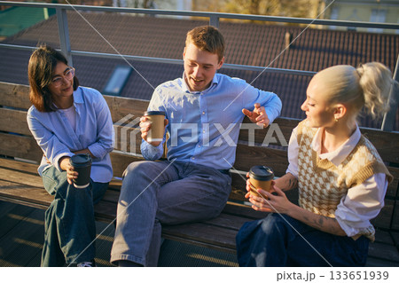 Coworkers sitting together on bench outdoors enjoying coffee and conversation Coworkers sitting together on bench outdoors enjoying coffee and conversation 133651939