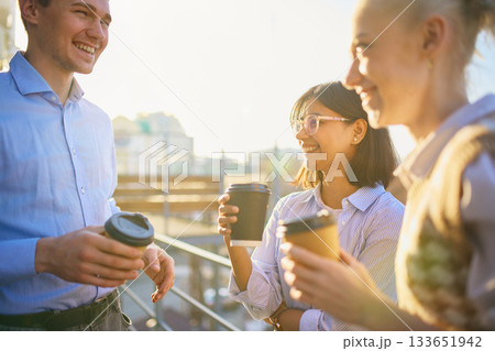 Coworkers enjoying takeaway coffee together outside in bright sunlight Coworkers enjoying takeaway coffee together outside in bright sunlight 133651942