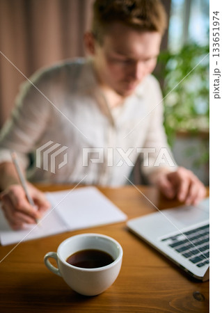 Coffee cup on desk as man writes notes and works in office 133651974
