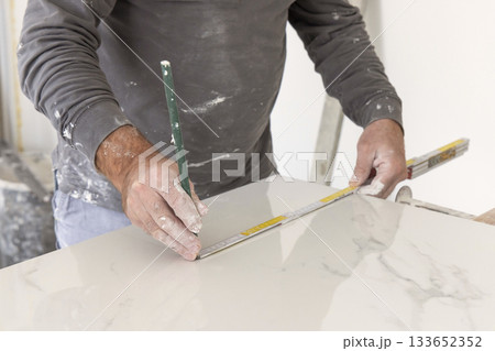 Craftman in grey shirt measures a marble tile using a ruler. Handy men at work, hands closeup Craftman in grey shirt measures a marble tile using a ruler. Handy men at work, hands closeup 133652352