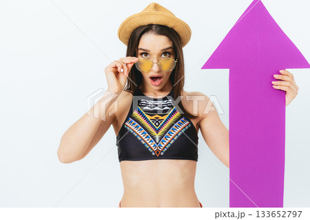 Woman in a bikini holding a pink paper with an arrow pointing upwards Woman in a bikini holding a pink paper with an arrow pointing upwards 133652797