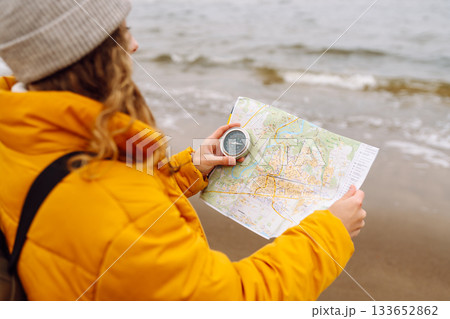 Traveler explorer young woman holding compass, map in hands on beach near the sea. Active lifestyle. Traveler explorer young woman holding compass, map in hands on beach near the sea. Active lifestyle. 133652862