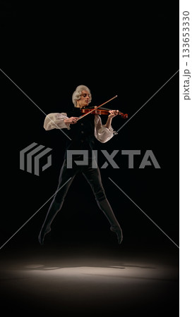 Violinist captured mid-jump playing expressive classical lines on dark stage. Violinist captured mid-jump playing expressive classical lines on dark stage. 133653330
