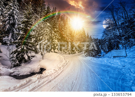 winter mountain landscape. day and night time change concept. empty winding road through fir forest covered with snow with sun and moon at twilight. duality and transition template winter mountain landscape. day and night time change concept. empty winding road through fir forest covered with snow with sun and moon at twilight. duality and transition template 133653794