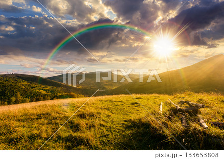 beautiful countryside at sunset. wonderful summertime landscape in mountains in evening light. scenic view of grassy field and rolling hills. rural scenery storytelling image under the rainbow 133653808