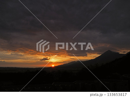 暗雲の下、磐梯山の麓に沈む夕日。シルエットの山とオレンジ色に輝く雲とのコントラストが印象的で綺麗だ。 暗雲の下、磐梯山の麓に沈む夕日。シルエットの山とオレンジ色に輝く雲とのコントラストが印象的で綺麗だ。 133653817