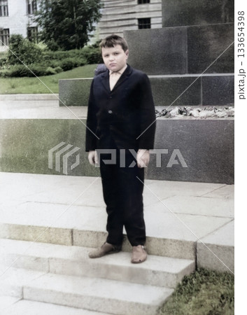A vintage portrait of a boy in a jacket and trousers at the foot of a monument with flowers. Retro photo from 1969. A vintage portrait of a boy in a jacket and trousers at the foot of a monument with flowers. Retro photo from 1969. 133654398