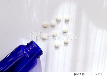 白背景に広がる錠剤と青色ボトルのヘルスケアイメージ 白背景に広がる錠剤と青色ボトルのヘルスケアイメージ 133654410