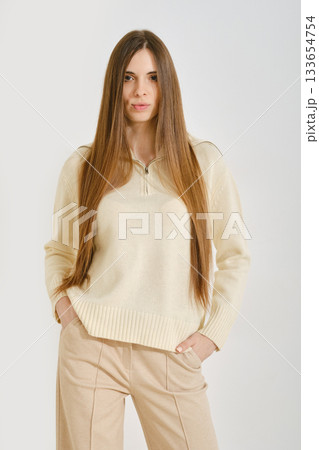 A woman in a cream sweater poses with her hands in pockets of beige pants A woman in a cream sweater poses with her hands in pockets of beige pants 133654754