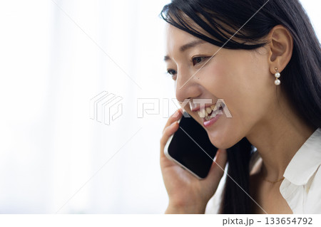 ノートパソコンで作業をしながらスマートフォンで電話する笑顔の若い女性 133654792