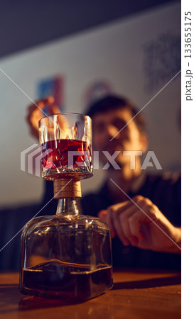 Glass of red drink balanced on bottle neck in bar setting 133655175