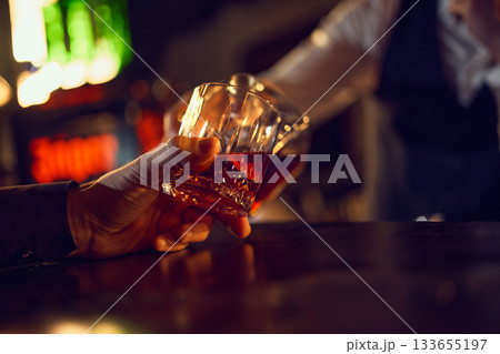 Close-up hands clinking whiskey glasses in dim bar. Close-up hands clinking whiskey glasses in dim bar. 133655197