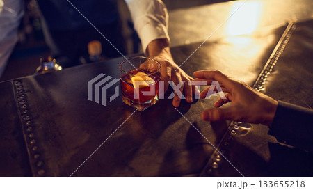 Bartender sliding finished dark drink with citrus peel toward customer Bartender sliding finished dark drink with citrus peel toward customer 133655218