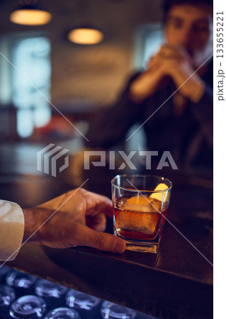 Bartender sliding amber drink toward thoughtful customer at bar 133655221