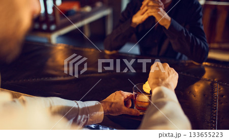 Bartender placing citrus garnish over iced dark drink while guest waits Bartender placing citrus garnish over iced dark drink while guest waits 133655223