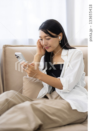 ワイヤレスイヤホンをつけてスマートフォンを見る笑顔の女性 133655418