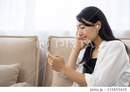 ワイヤレスイヤホンをつけてスマートフォンを見る笑顔の女性 ワイヤレスイヤホンをつけてスマートフォンを見る笑顔の女性 133655420