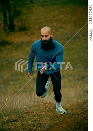 Male runner climbing steep hill with steady controlled stride Male runner climbing steep hill with steady controlled stride 133655489
