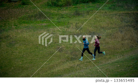 Two runners moving through wide grassy hillside trail 133655495