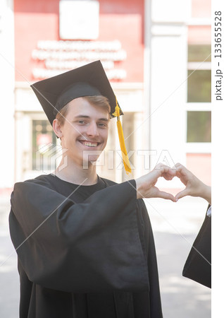 Young Caucasian man in graduation gown showing heart sign.  133655528
