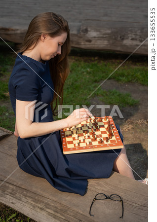 Caucasian woman playing chess outdoors. Caucasian woman playing chess outdoors. 133655535