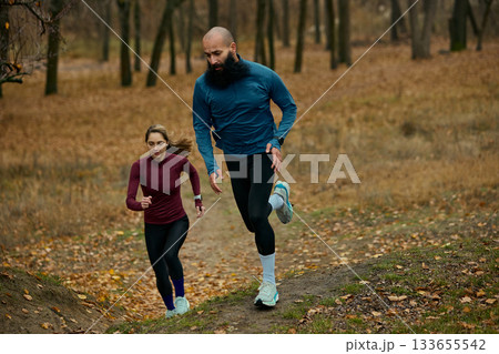 Runners powering uphill on forest trail during intense autumn training 133655542