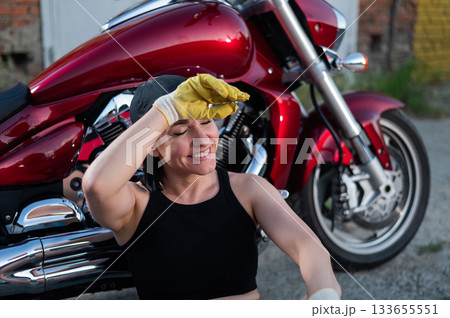 Brunette woman repairs a red motorcycle. Brunette woman repairs a red motorcycle. 133655551