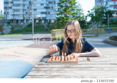 Caucasian woman playing chess outdoors. Caucasian woman playing chess outdoors. 133655590