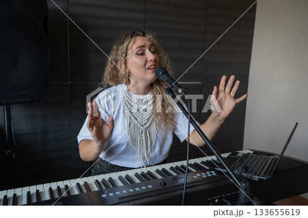 Caucasian woman singing into microphone and playing synthesizer and recording herself on laptop. Caucasian woman singing into microphone and playing synthesizer and recording herself on laptop. 133655619