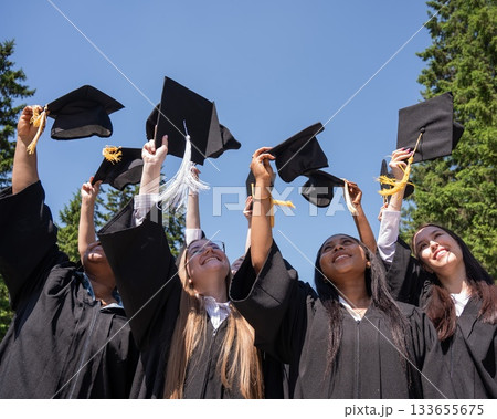 Young women of different nationalities pull graduation caps up.  133655675