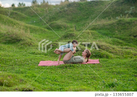 Caucasian woman doing yoga with her little son outdoors.  133655807