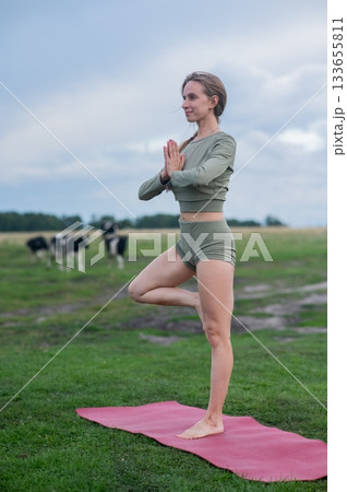 Caucasian woman doing yoga in rural area among herd of cows.  133655811