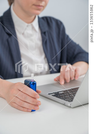Business woman smoking an electronic cigarette while working on a laptop. Tobacco heating system. Business woman smoking an electronic cigarette while working on a laptop. Tobacco heating system. 133655862