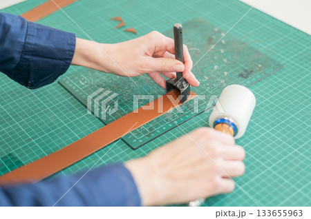 Woman tanner processes the edges of a leather belt in a workshop.  133655963