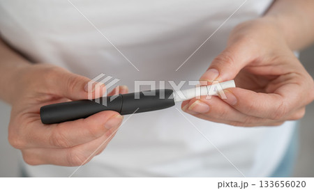 A woman inserts a cigarette stick into a tobacco heating system. Electronic cigarette. 133656020