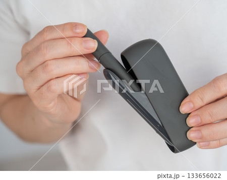 A woman takes a tobacco heating system out of a charger. Electronic cigarette. 133656022