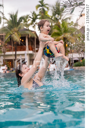 Caucasian woman holds son while swimming in pool on vacation. Caucasian woman holds son while swimming in pool on vacation. 133656237