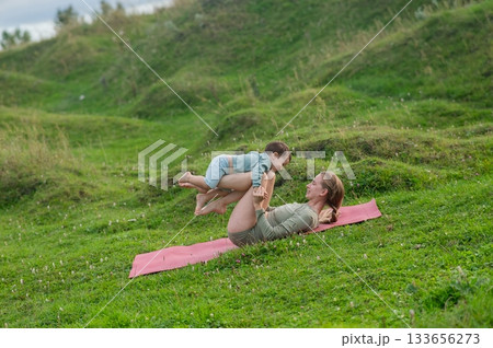 Caucasian woman doing yoga with her little son outdoors.  133656273