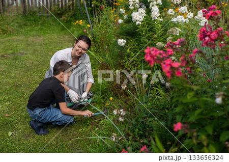 Caucasian woman and her son watering flowers in the garden.  133656324