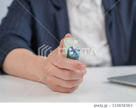 Business woman smoking an electronic cigarette while working on a laptop. Tobacco heating system.  133656363