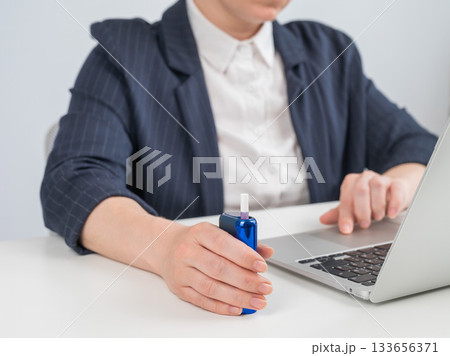 Business woman smoking an electronic cigarette while working on a laptop. Tobacco heating system. Business woman smoking an electronic cigarette while working on a laptop. Tobacco heating system. 133656371
